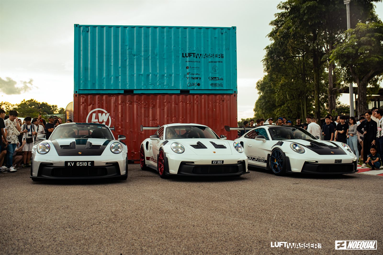 Three white 992 GT3s parked in front of the stacked Luftwasser shipping containers